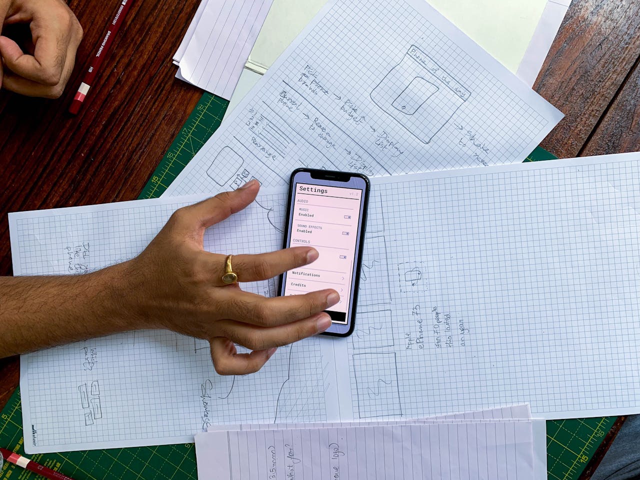 Hand holding smartphone over app design sketches on papers, top view.